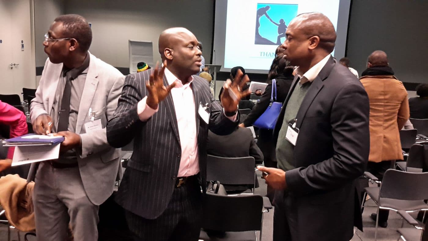 Three attendees standing and talking at the front of the room