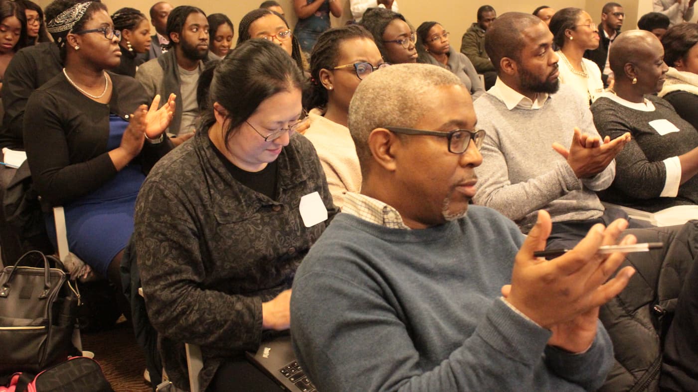 Two attendees talking in a full room of seated guests