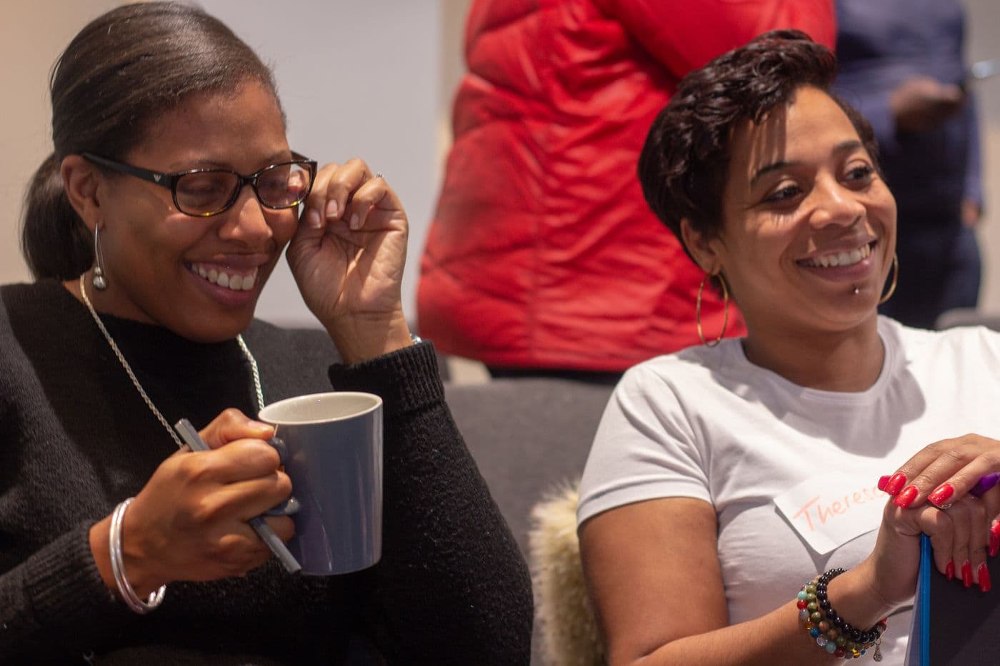 Two attendees laughing together over a hot drink