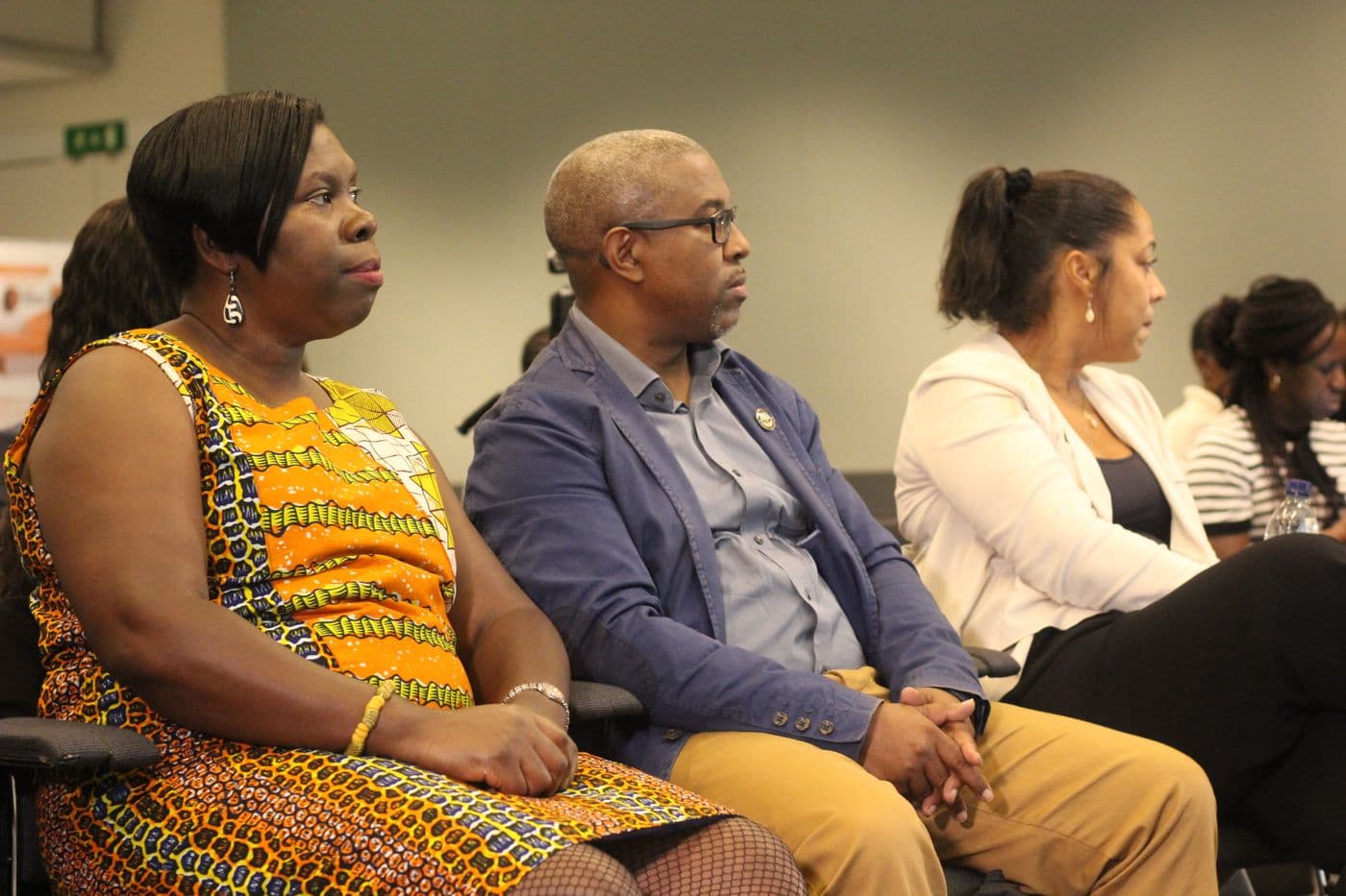 Three attendees listening from the front row