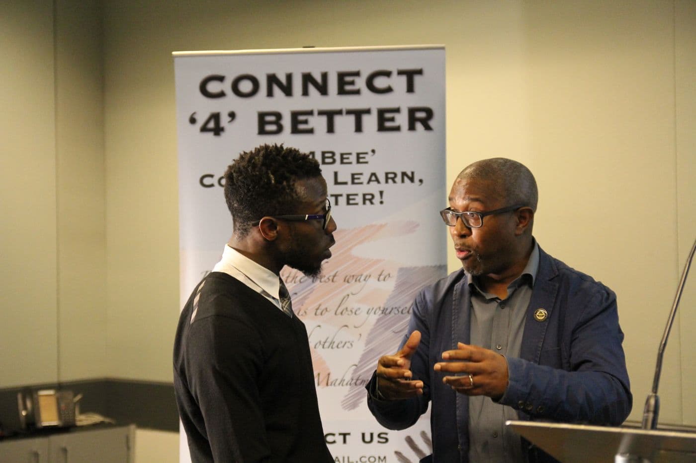 Two attendees talking beside the Connect ’4’ Better banner